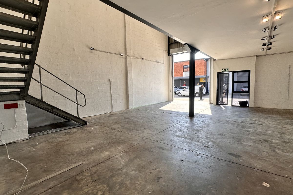 Open-plan industrial utility space featuring concrete flooring, a metal staircase, and track lighting, suitable for a workshop, showroom, or creative studio.