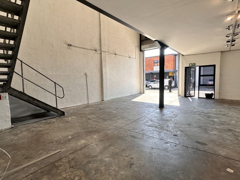 Open-plan industrial utility space featuring concrete flooring, a metal staircase, and track lighting, suitable for a workshop, showroom, or creative studio.