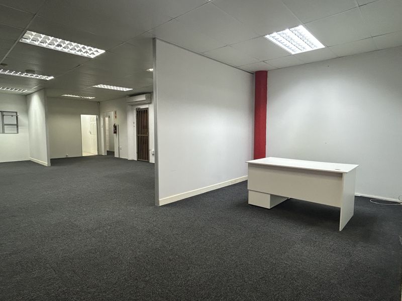 Open-plan office space featuring neutral carpeting, suspended ceilings with recessed lighting, and a partition wall for flexible workspace configuration.