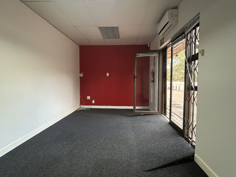 An empty office space featuring dark carpeting, a split-system air conditioner, and a glass door with a security gate leading to an outdoor area.