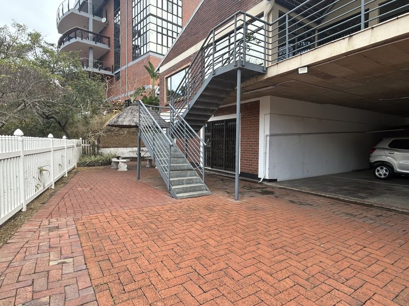 Rear exterior view of the office property featuring brick paving, a metal staircase leading to the upper level, and a covered parking area.