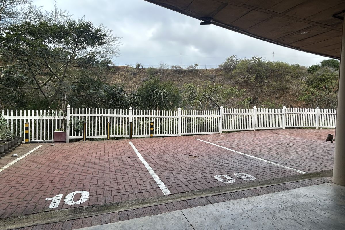 Covered parking area featuring numbered paved bays and a white picket fence boundary overlooking a natural embankment.