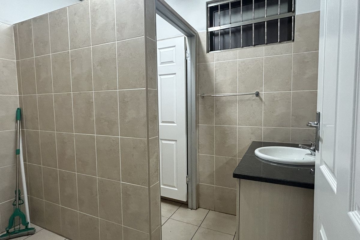 A functional bathroom featuring tiled walls and flooring, a vanity cabinet with a countertop basin, and a window with security bars.
