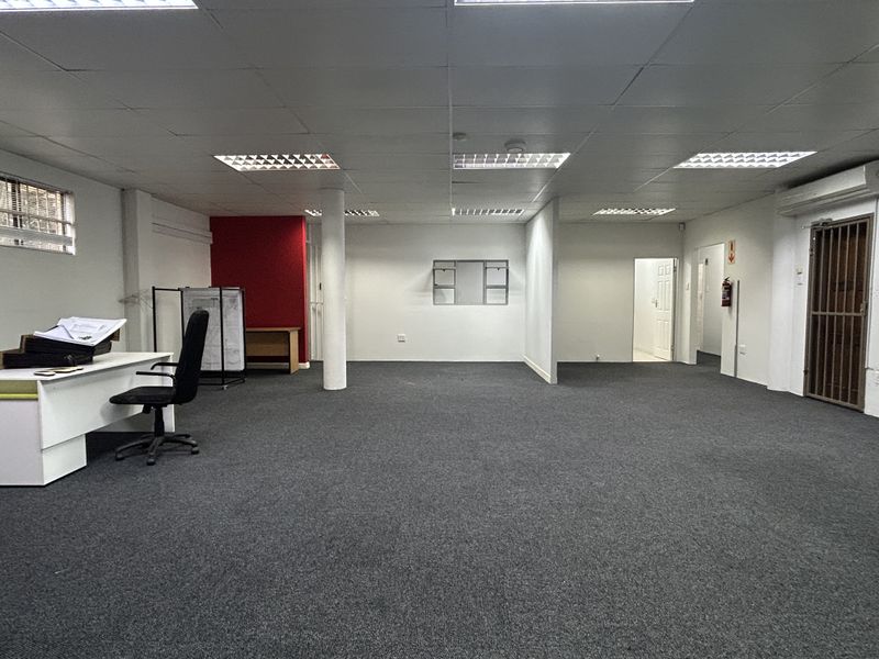 Open-plan office space featuring a suspended ceiling with recessed lighting, carpeted flooring, and a secure entrance gate.
