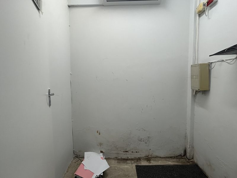 A small utility or storage space featuring an electrical distribution board, wall-mounted air conditioning unit, and visible wear to the lower wall surfaces.