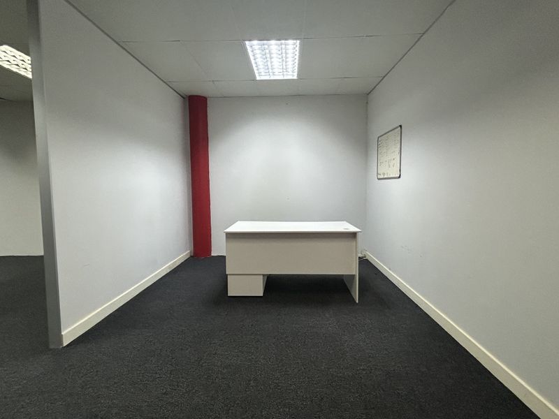 A functional office space featuring dark carpeting, a prominent structural column, and recessed ceiling lighting.