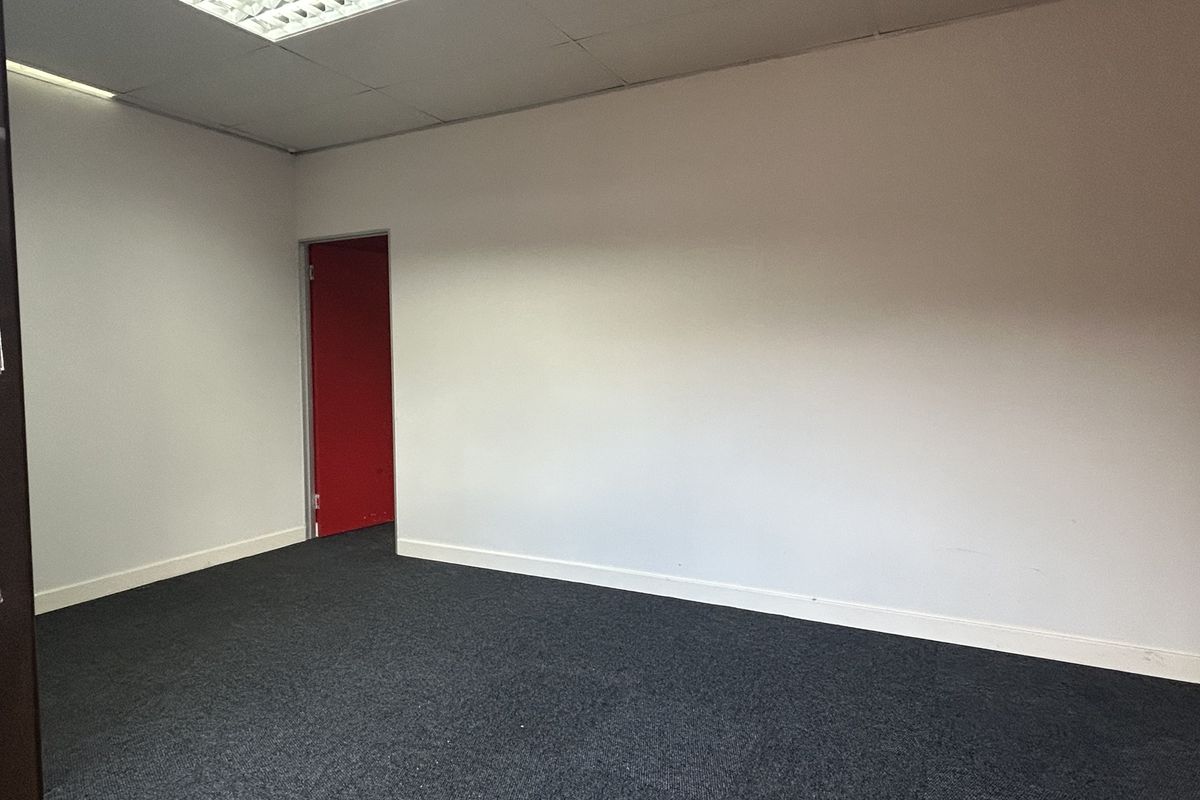 A clean, empty office space featuring dark carpeting, white walls, and recessed ceiling lighting, providing a versatile environment for professional use.