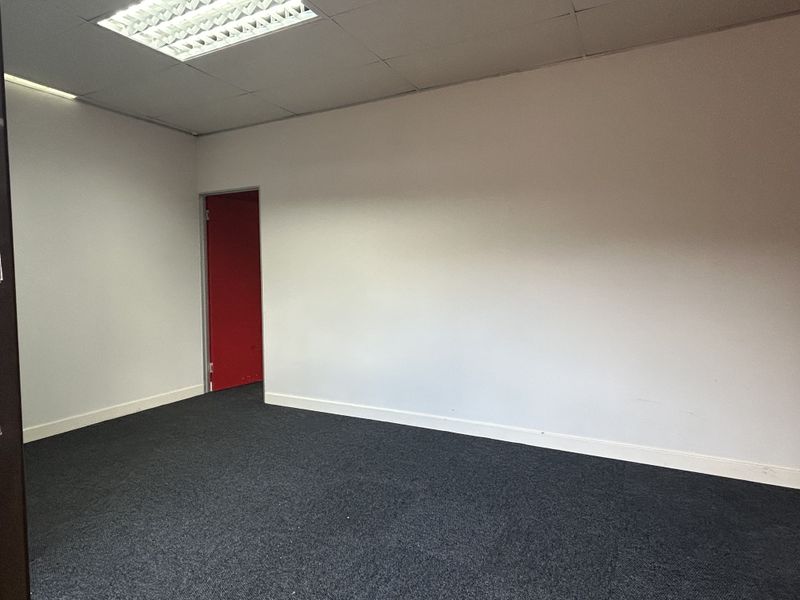 A clean, empty office space featuring dark carpeting, white walls, and recessed ceiling lighting, providing a versatile environment for professional use.