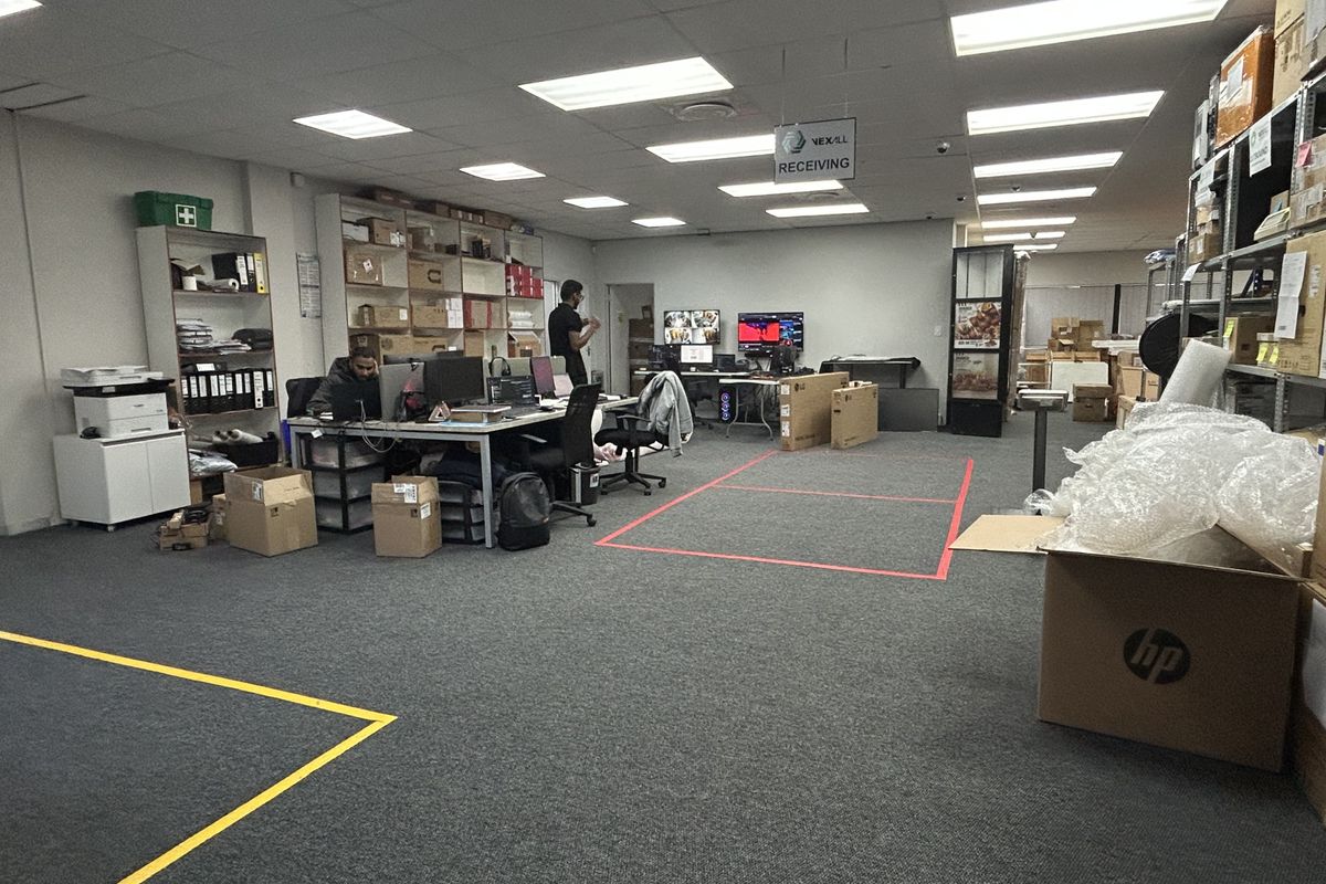A functional commercial office space featuring suspended ceilings, recessed lighting, and carpeted flooring, currently utilized as a receiving and administrative work area.