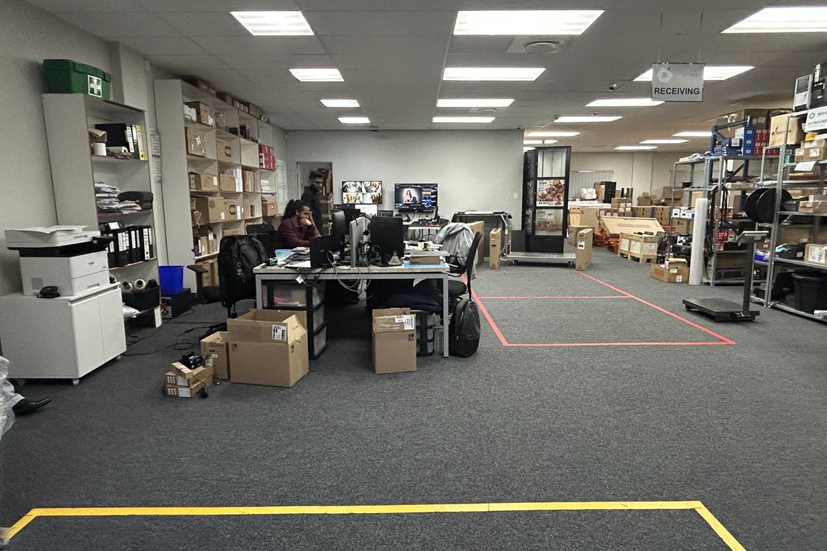 A functional commercial utility and receiving area featuring suspended ceilings, recessed lighting, carpeted flooring, and integrated industrial storage racking.