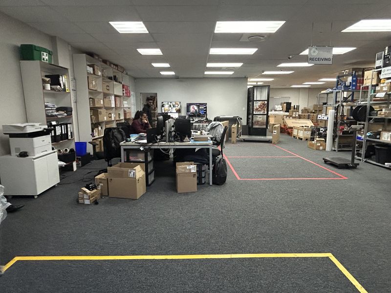 A functional commercial utility and receiving area featuring suspended ceilings, recessed lighting, carpeted flooring, and integrated industrial storage racking.