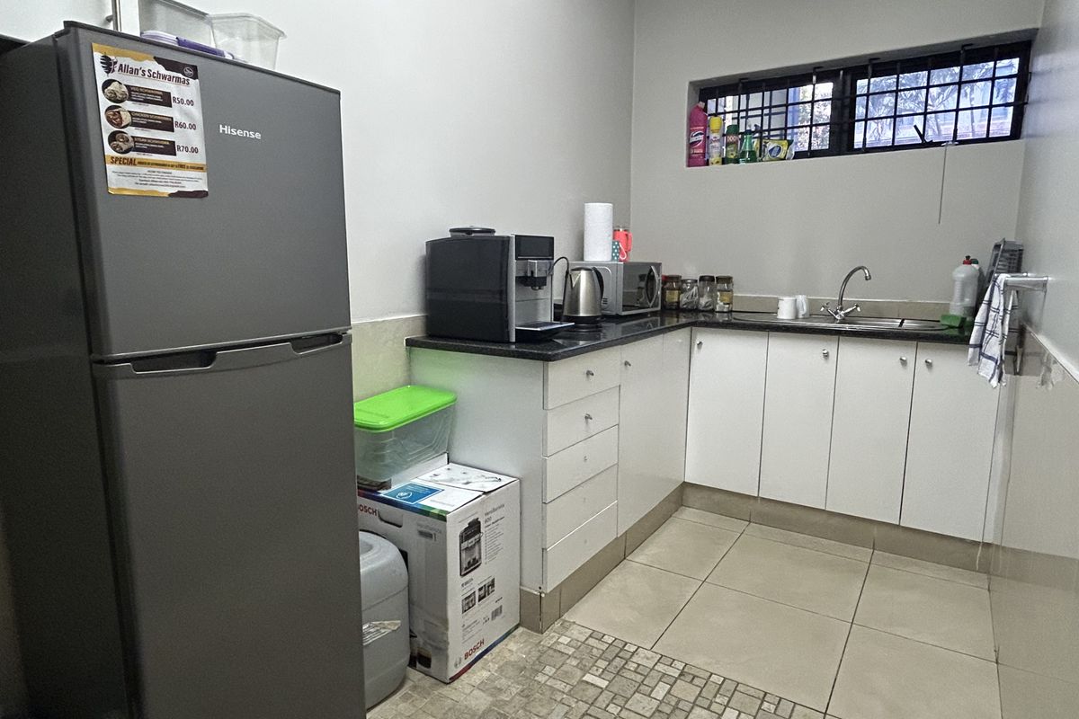 A compact kitchen area featuring white built-in cabinetry, granite countertops, a stainless steel sink, and tiled flooring with security bars on the window.