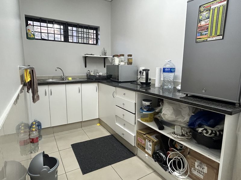 Functional scullery area featuring granite countertops, white cabinetry, stainless steel sink, and tiled flooring with security bars on the window.