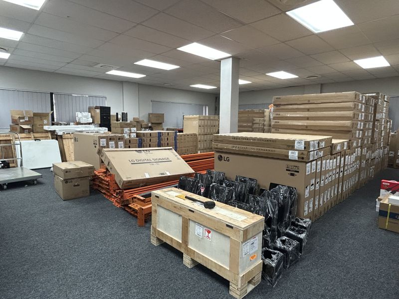 A commercial utility or storage space featuring a suspended ceiling, recessed lighting, and carpeted flooring, currently utilized for inventory storage.