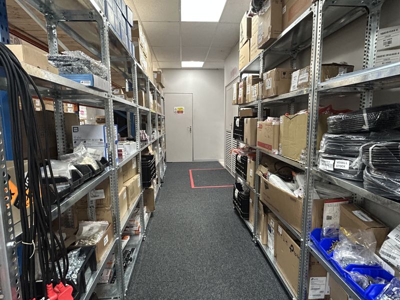 A functional commercial storage or utility room featuring organized metal shelving units, a drop ceiling with recessed lighting, and a secure access door.