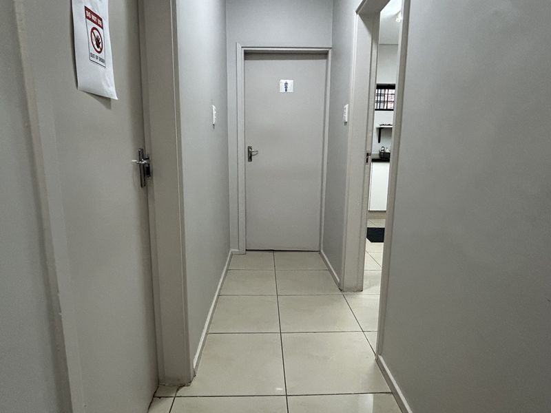 A functional commercial hallway with tiled flooring and multiple internal doors leading to various rooms, including a restroom.