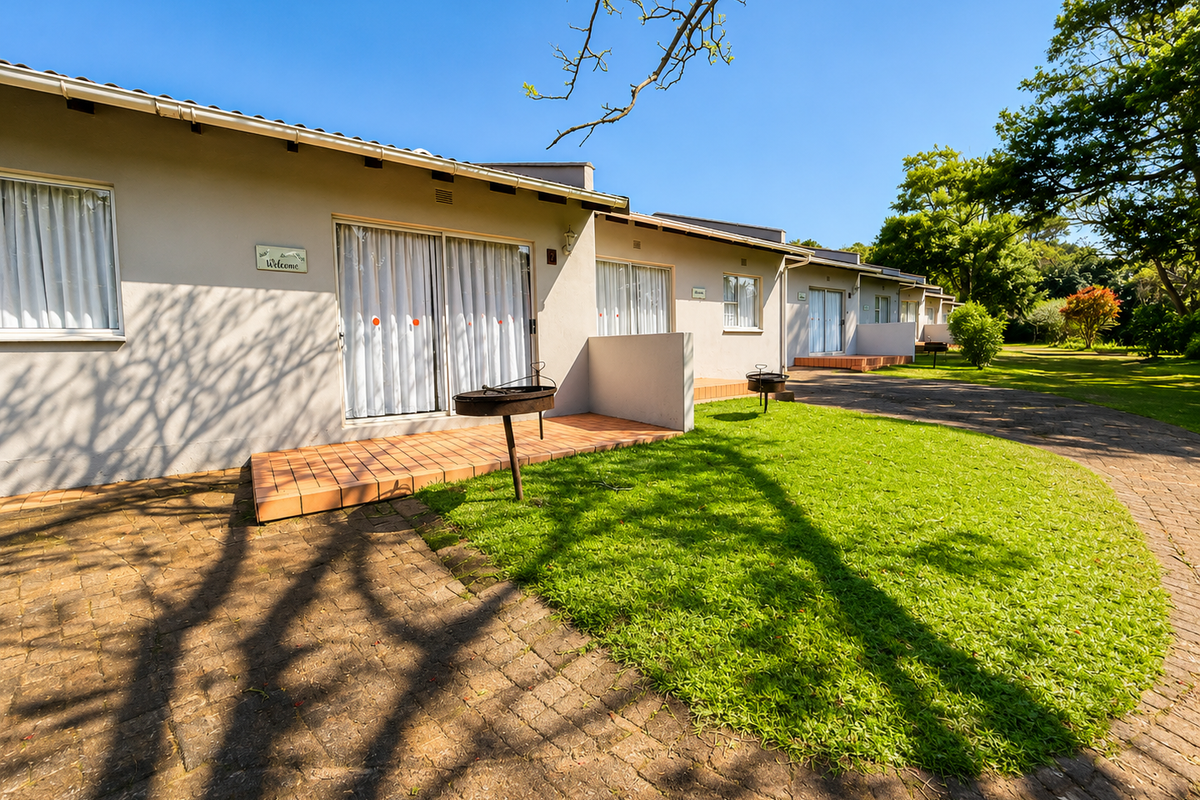 A row of lodge units featuring individual tiled patios, sliding glass doors, and access to a well-maintained garden and paved driveway area.
