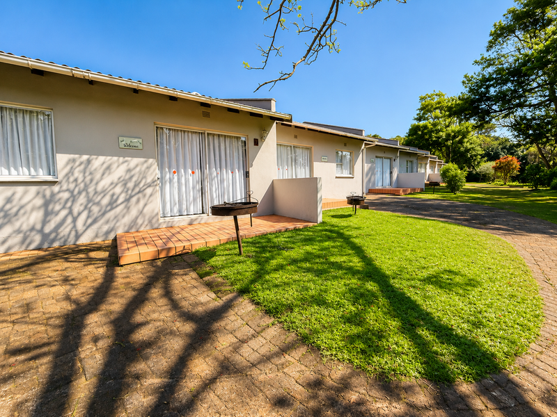 A row of lodge units featuring individual tiled patios, sliding glass doors, and access to a well-maintained garden and paved driveway area.