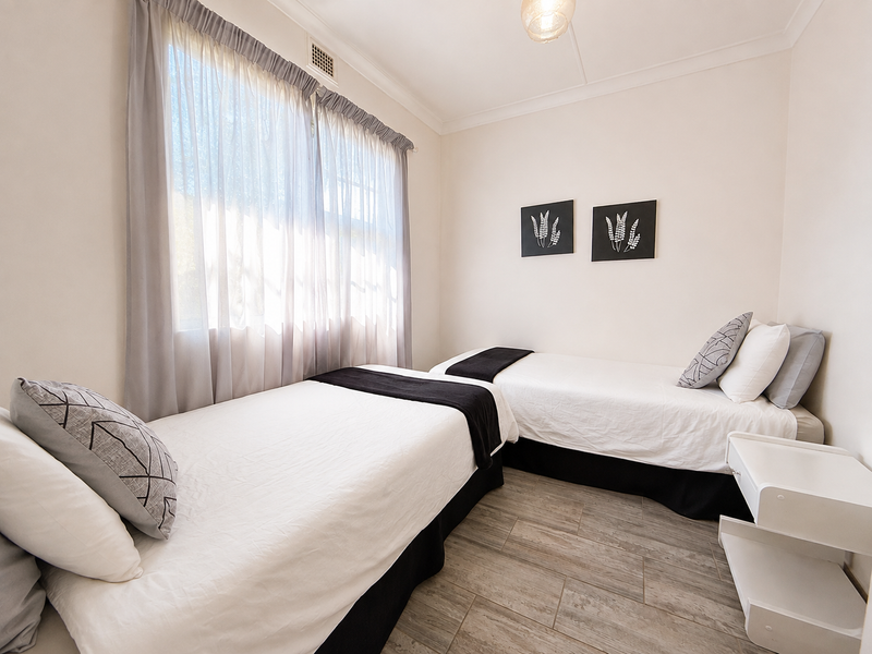 A well-maintained bedroom featuring neutral walls, tiled flooring, and a ceiling-mounted air conditioning vent, providing a clean and functional living space.