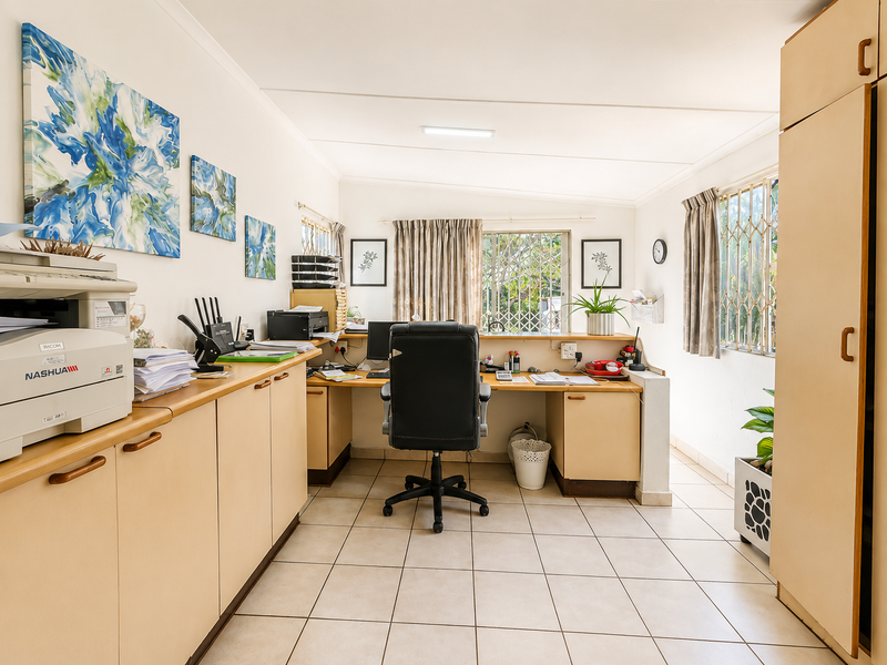 A functional home office featuring built-in cabinetry, a spacious desk area, tiled flooring, and security bars on the windows.