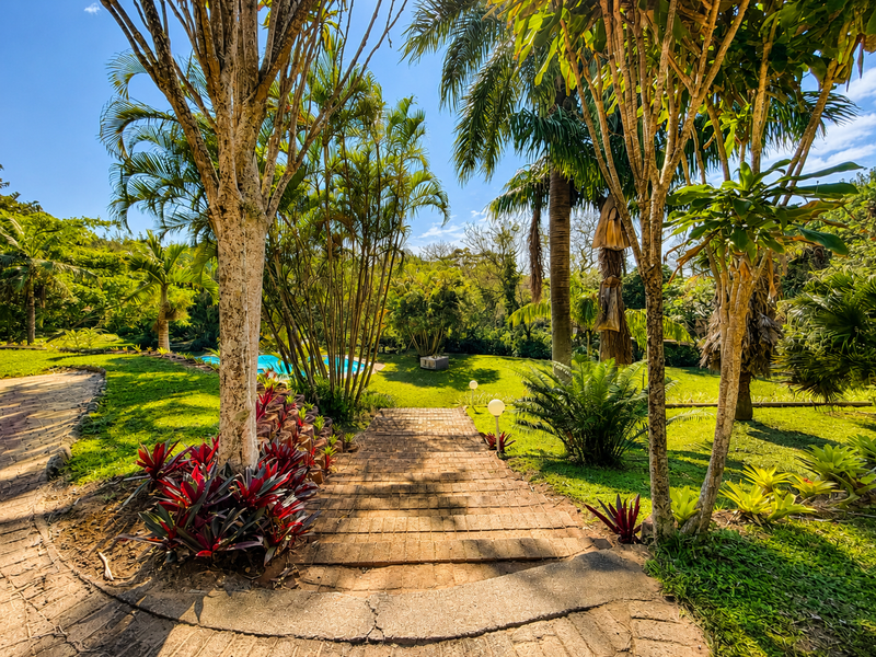 A lush, well-maintained garden featuring a brick-paved pathway leading through mature trees and landscaped greenery.