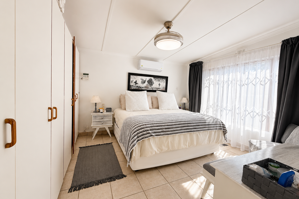A well-maintained bedroom featuring built-in cupboards, tiled flooring, a ceiling fan, and a split-system air conditioner for climate control.