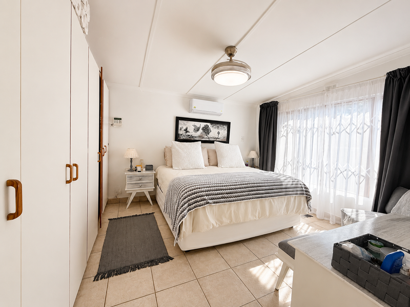 A well-maintained bedroom featuring built-in cupboards, tiled flooring, a ceiling fan, and a split-system air conditioner for climate control.