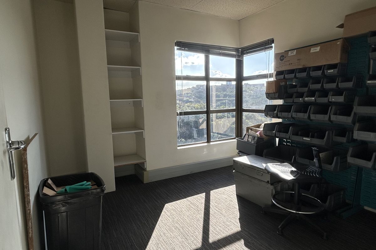 A functional office space featuring built-in shelving, a corner window with natural light, and carpeted flooring, suitable for a professional workspace.