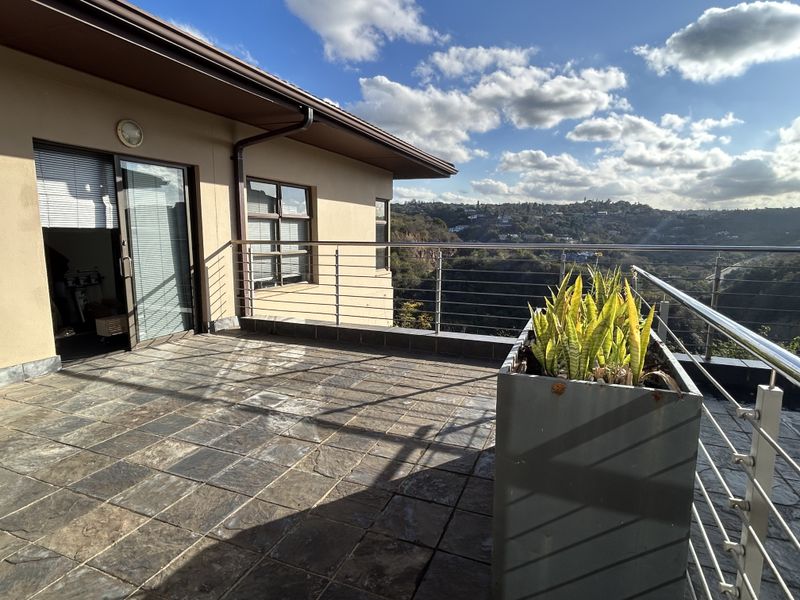 Spacious balcony featuring slate tile flooring and a stainless steel balustrade, offering expansive elevated views of the surrounding landscape.