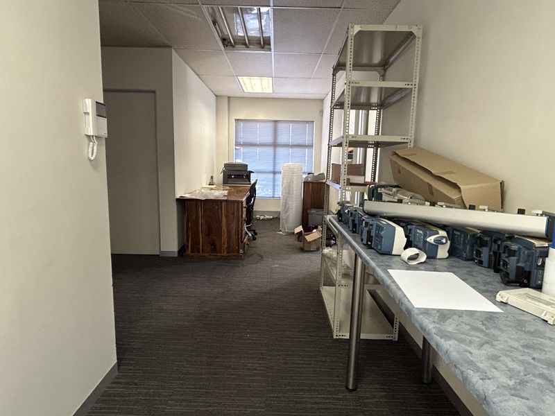 A functional office space featuring a suspended ceiling, recessed lighting, and carpeted flooring, currently utilized for storage and workspace.