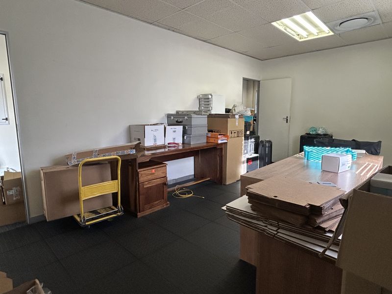 A functional office space featuring a suspended ceiling with recessed lighting and dark carpet tiles, currently utilized for storage.