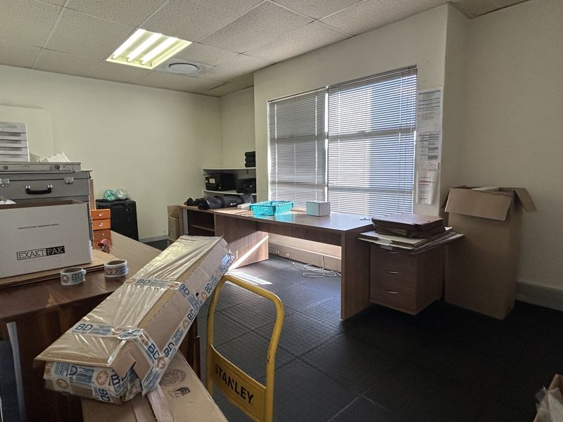 A functional office space featuring carpet tiles, a built-in desk, and large windows with venetian blinds, providing a practical workspace environment.