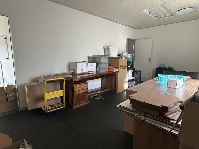 A functional office space featuring a suspended ceiling with recessed lighting and dark carpet tiles, currently utilized for storage.