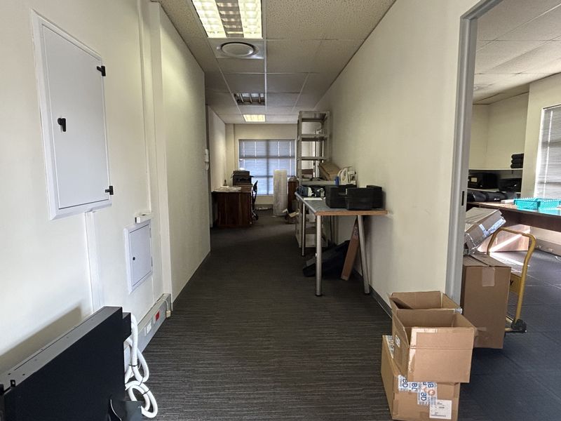 A functional office hallway featuring suspended ceilings, recessed lighting, and carpeted flooring, providing access to adjacent workspace areas.