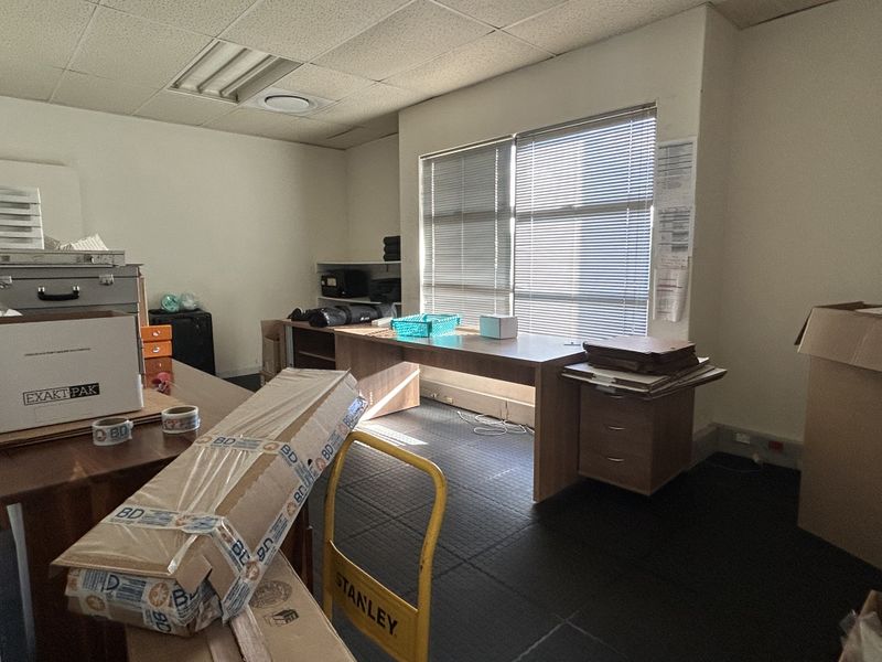 A functional office space featuring a built-in desk, venetian blinds, and recessed lighting, currently used for storage.