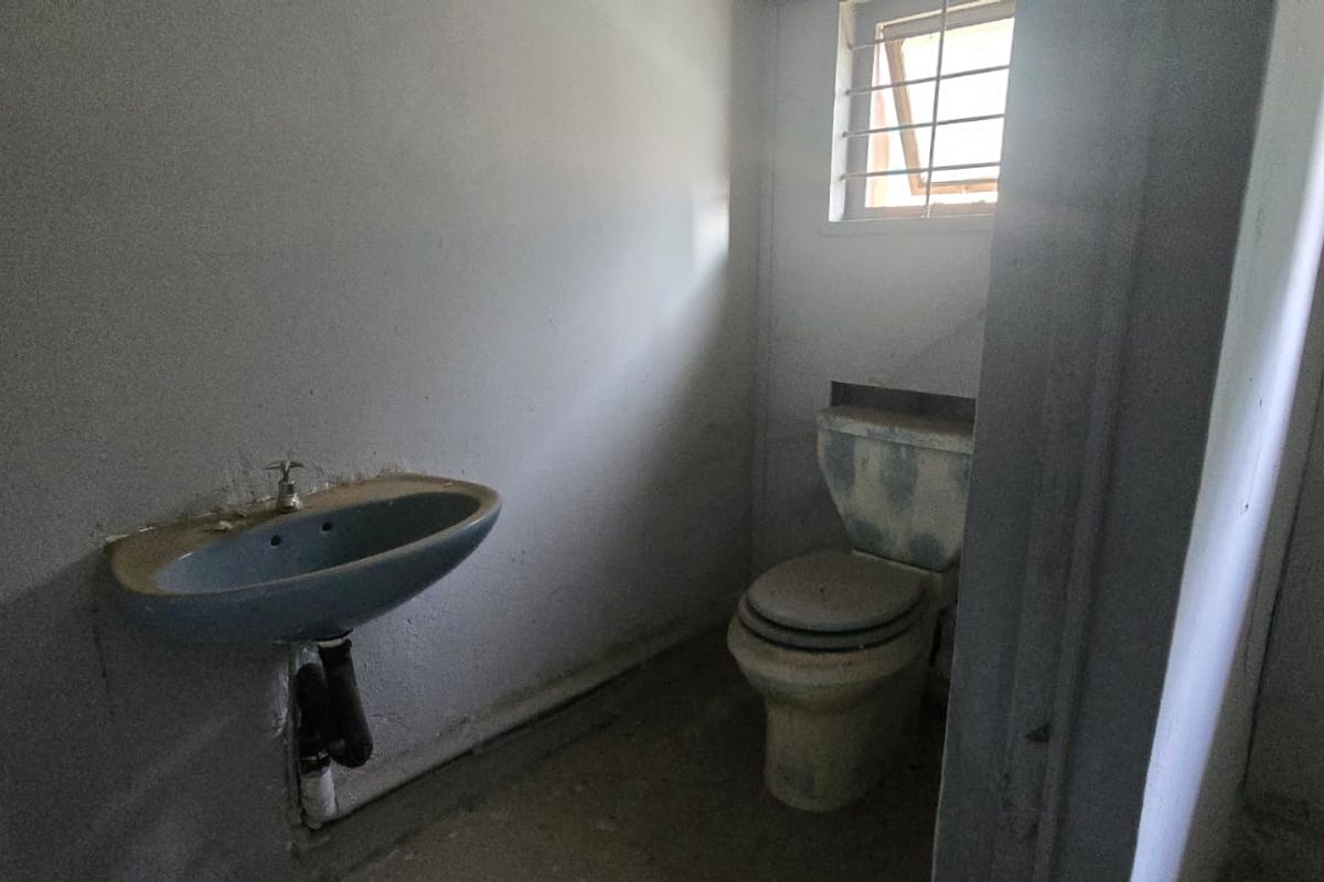 A small, dated bathroom featuring a wall-mounted basin and toilet, requiring significant refurbishment and cosmetic updates to improve functionality and appearance.