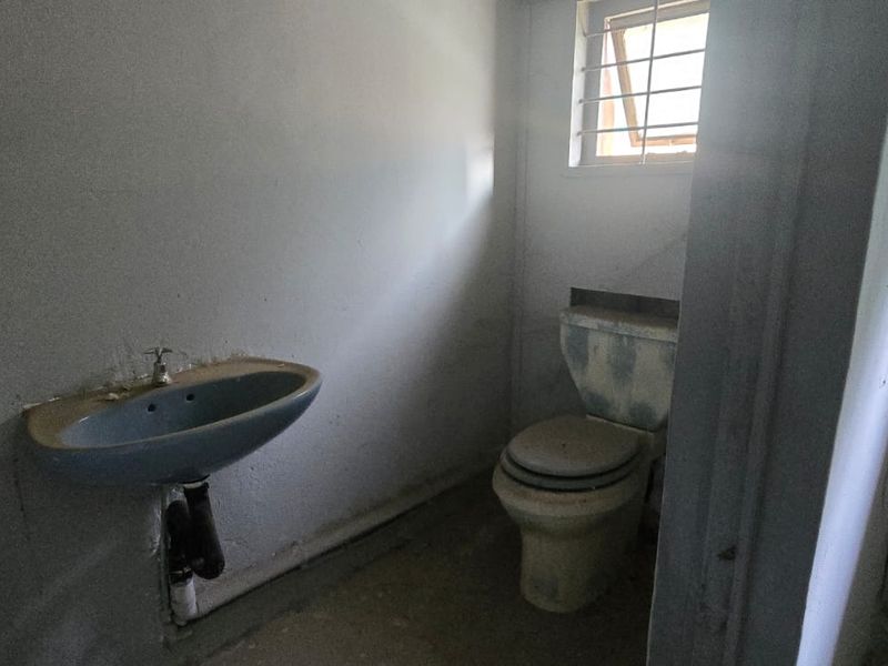 A small, dated bathroom featuring a wall-mounted basin and toilet, requiring significant refurbishment and cosmetic updates to improve functionality and appearance.