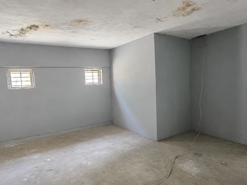 An empty utility space featuring concrete flooring, security bars on windows, and visible ceiling water damage requiring maintenance.