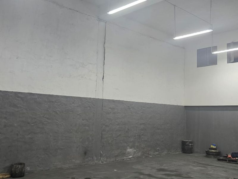Spacious industrial utility area featuring high ceilings, concrete flooring, and functional overhead fluorescent lighting, suitable for storage or workshop use.