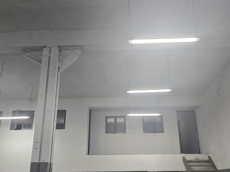 Industrial utility space featuring high ceilings, suspended lighting, a steel support column, and a mezzanine level, suitable for storage or workshop use.