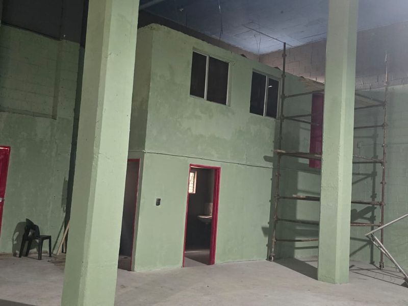 Spacious industrial utility area featuring high ceilings, concrete structural columns, a mezzanine level, and a metal staircase, suitable for workshop or storage use.