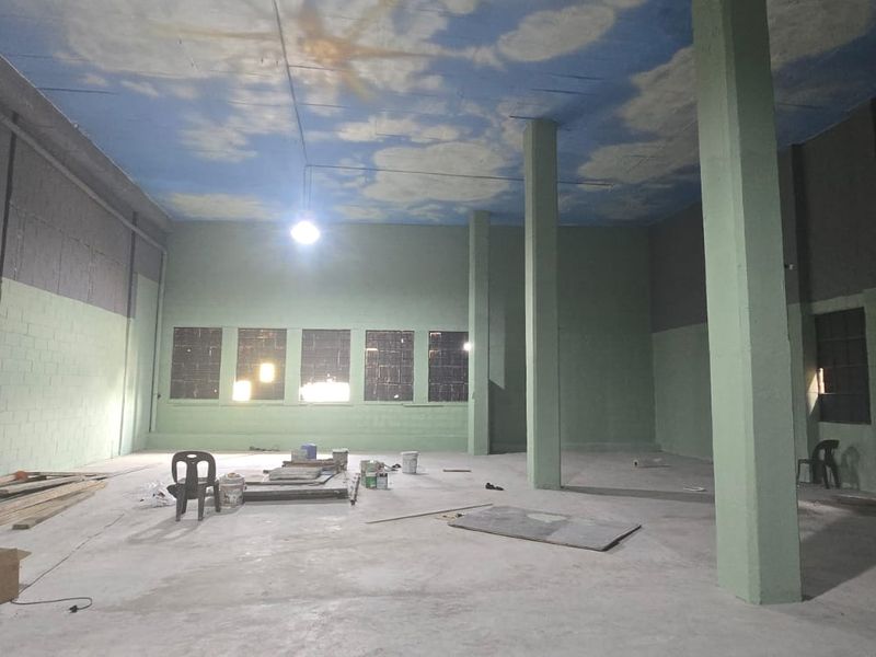 A large, open-plan industrial utility space featuring concrete flooring, structural columns, and painted blockwork walls with a decorative cloud-painted ceiling.