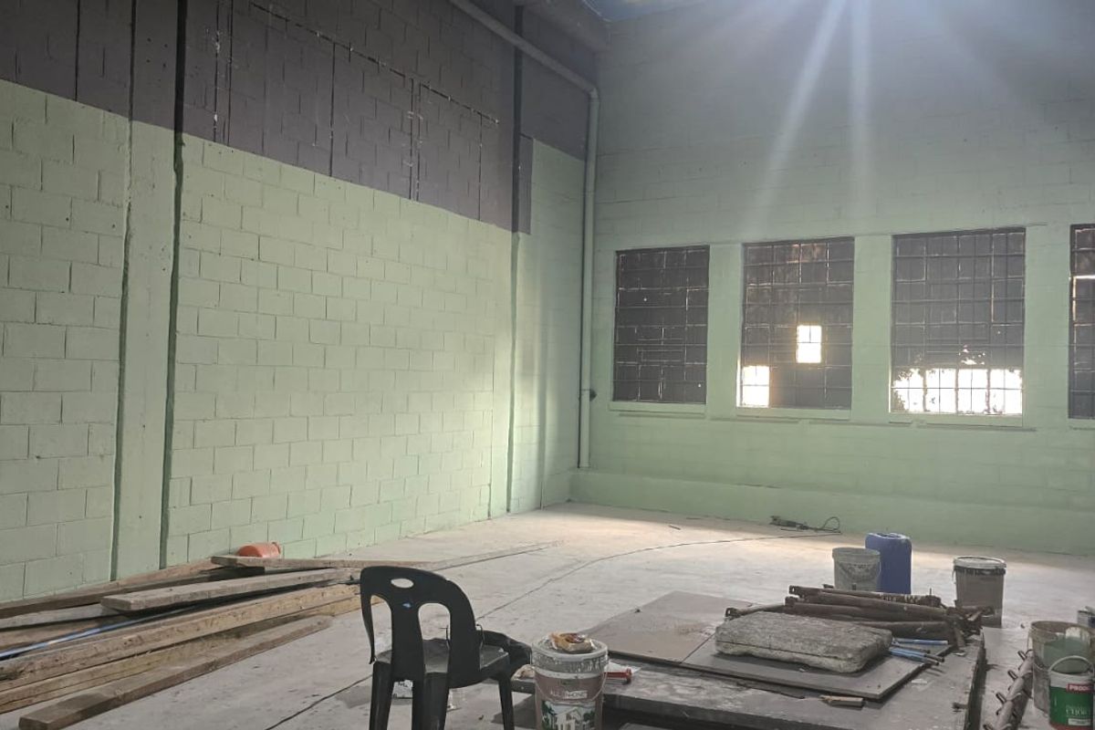 Spacious industrial utility area featuring exposed concrete block walls, high ceilings, and large grid windows, offering a versatile blank canvas for renovation.