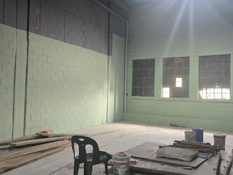 Spacious industrial utility area featuring exposed concrete block walls, high ceilings, and large grid windows, offering a versatile blank canvas for renovation.