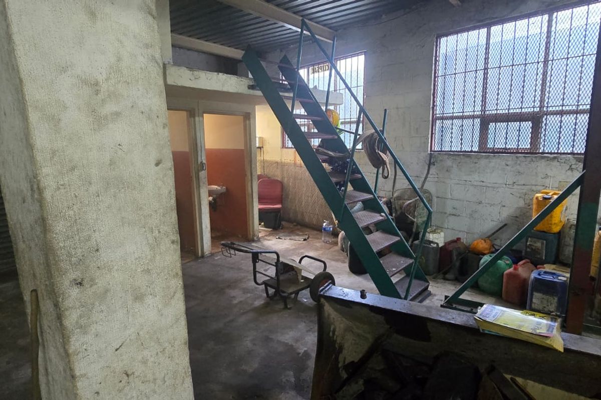 Industrial utility space featuring a metal staircase, mezzanine level, roller shutter door, and security-barred windows with exposed concrete block walls.