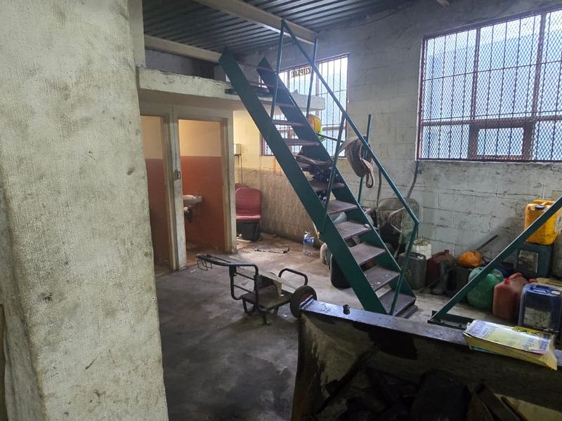 Industrial utility space featuring a metal staircase, mezzanine level, roller shutter door, and security-barred windows with exposed concrete block walls.