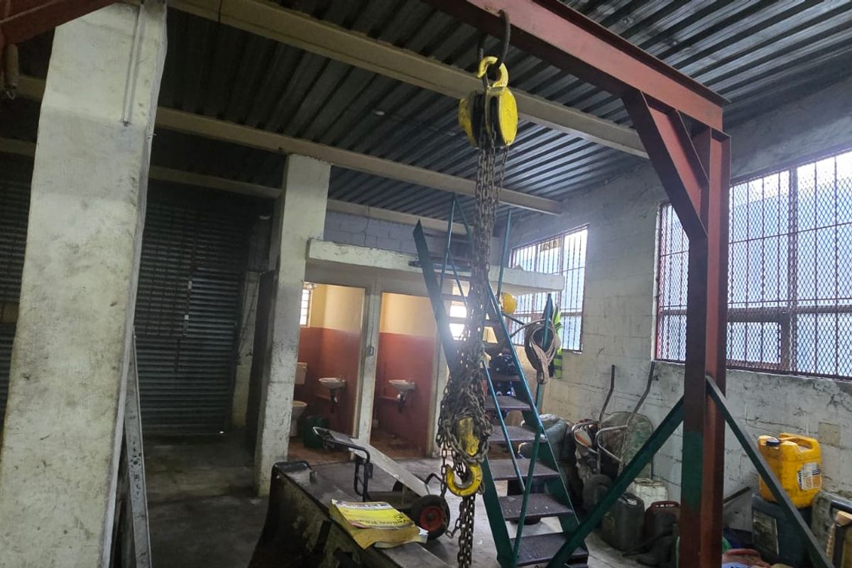 Industrial utility space featuring a heavy-duty overhead chain hoist, steel structural framing, concrete block walls, and secure barred windows.