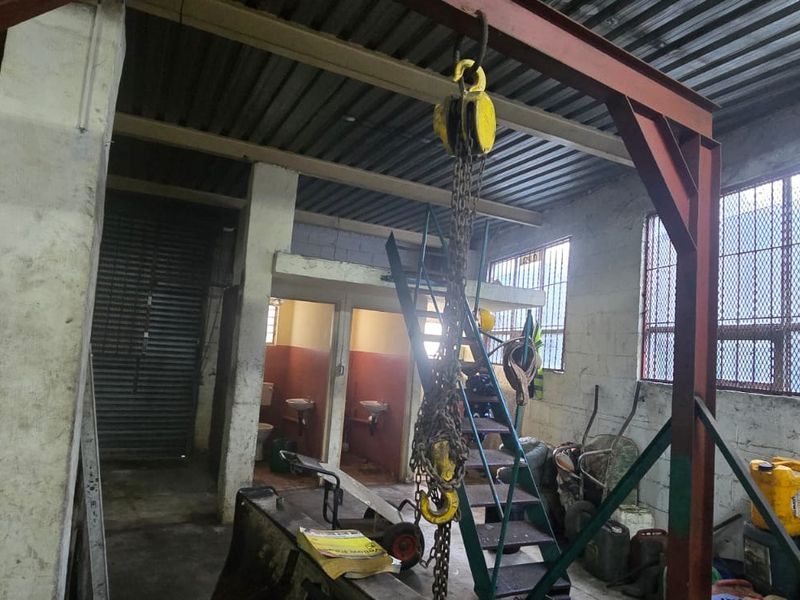Industrial utility space featuring a heavy-duty overhead chain hoist, steel structural framing, concrete block walls, and secure barred windows.