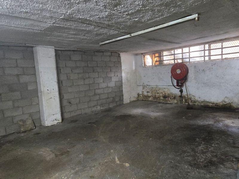 Industrial garage space featuring concrete block walls, a fire hose reel, and a security-grille window, showing signs of wear and damp.