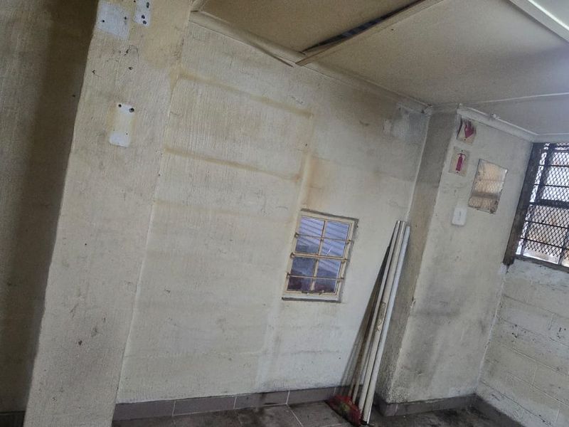An industrial utility space featuring exposed concrete block walls, security bars on windows, and basic fluorescent lighting, requiring maintenance and cosmetic updates.